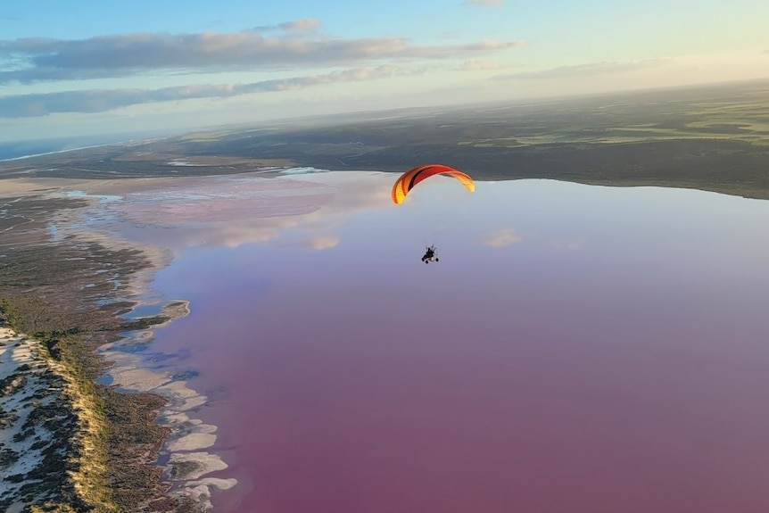 A paramotor flies over a spectacular lake.
