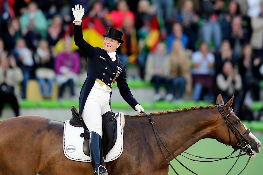 Isabell Werth waves to the crowd as she rides a chesnut mare.