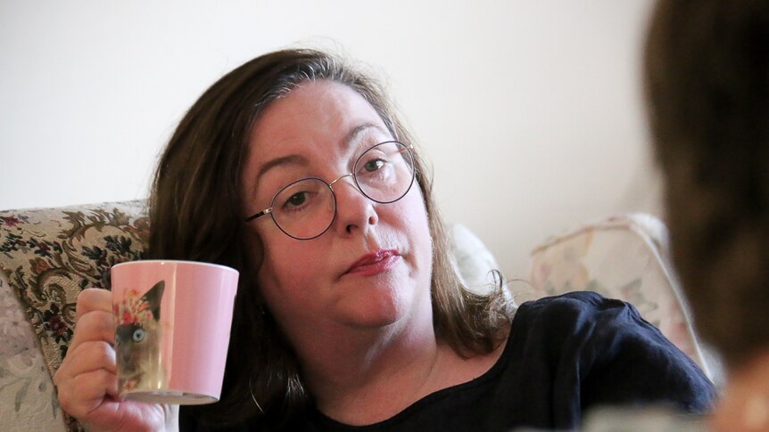 Jacki Whittaker sips tea while sitting on a couch in her living room