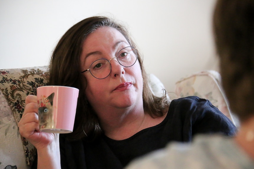 Jacki Whittaker sips tea while sitting on a couch in her living room