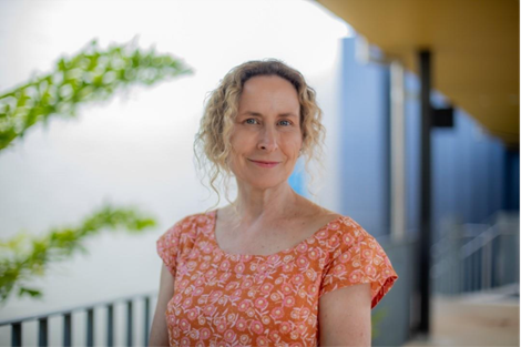 A middle aged lady with blonde curly hair in a short sleeved orange  top 