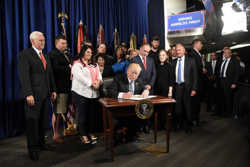 US President Donald Trump signing documents surrounded by a group of people from the United States Department of Veteran Affairs