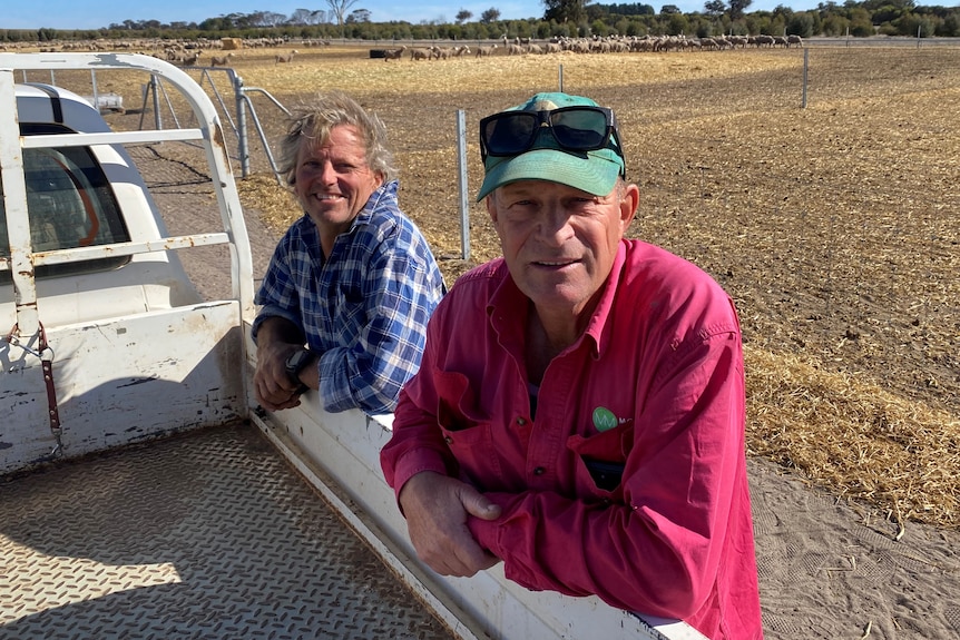 Two farmers leaning against a ute.