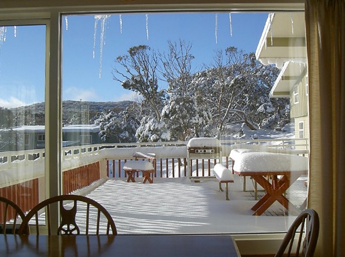 Looking out a window to a deck covered in snow.