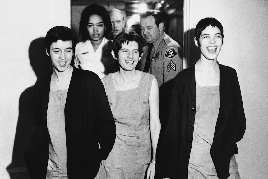 A black and white image of three women with short hair and matching dresses smilin as they leave a courtroom.