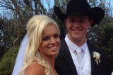 A blonde woman in a wedding dress and a man in a hat and suit.