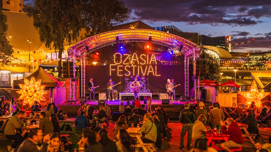 A large outdoor stage lit with neon lights and lanterns. The words "OzAsia Festival" adorn the stage in neon orange..