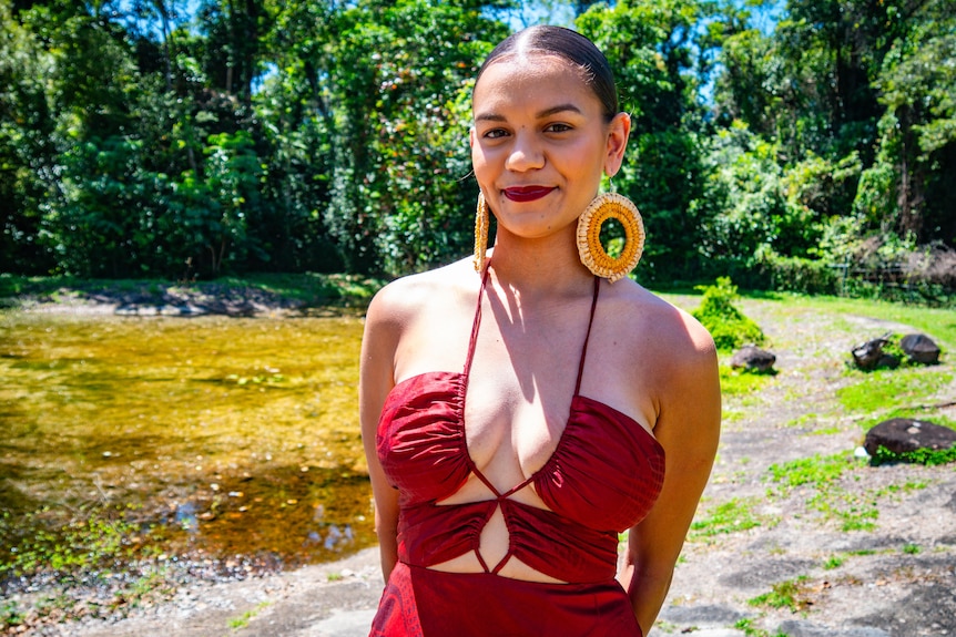 girl in red dress and earrings beside a pond.