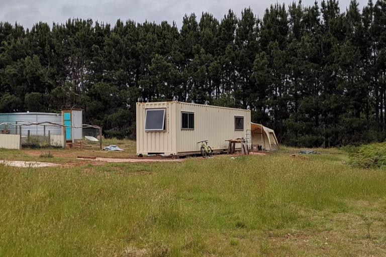 A sea container with windows cut out of it in a paddock. A tent can be partly seen at the back of the container