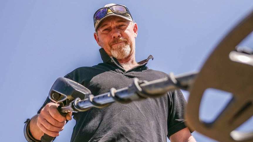 Coin Collector Dave Knox looks down at the camera whilst holding his metal detector.