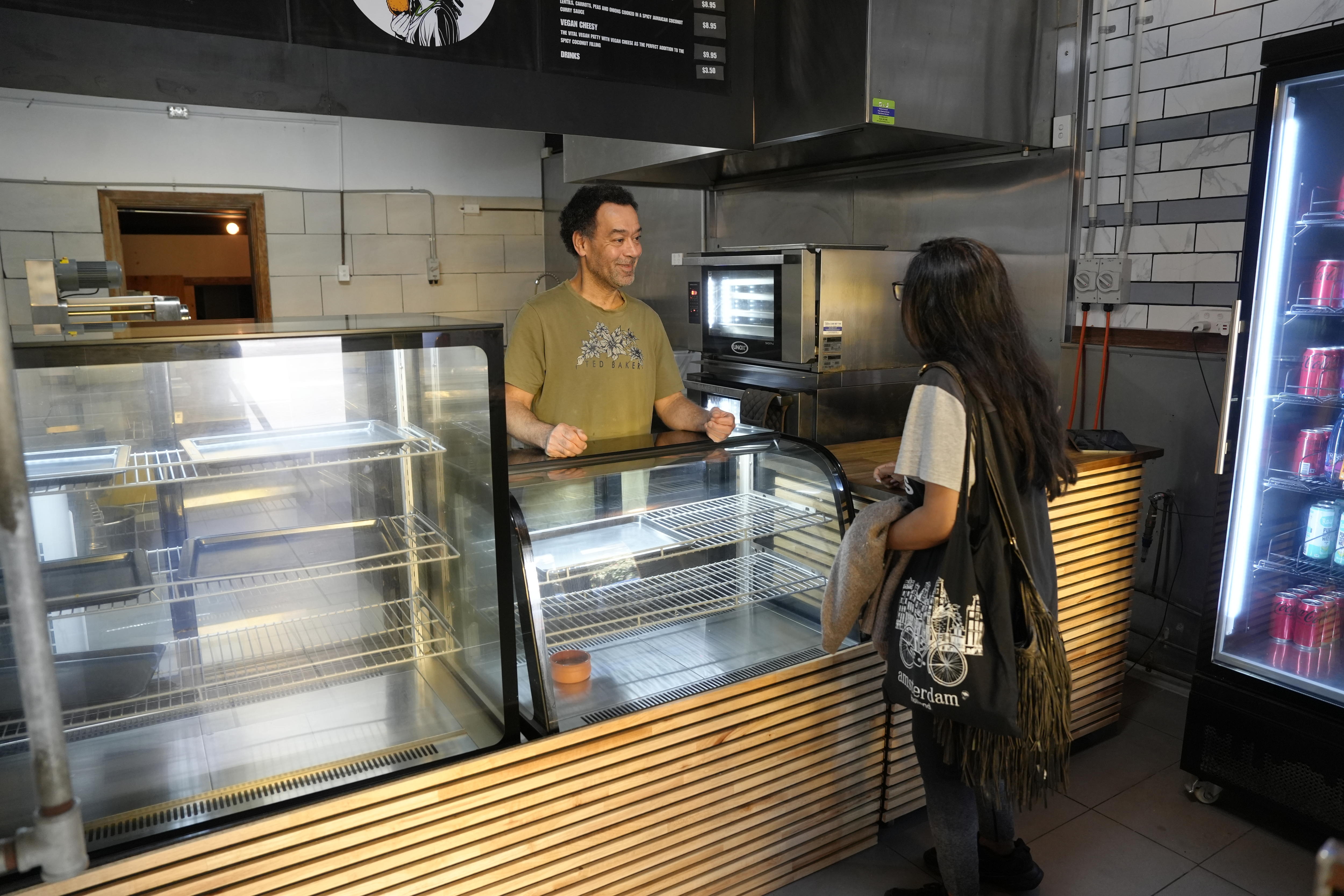 inside the Jamaican Patty Bakehouse with owner standing  behind the counter talking to a female customer