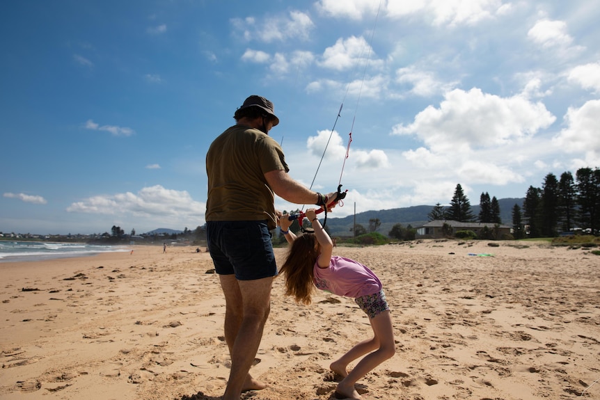 A man helps a young girl hold the handle of a large kite.
