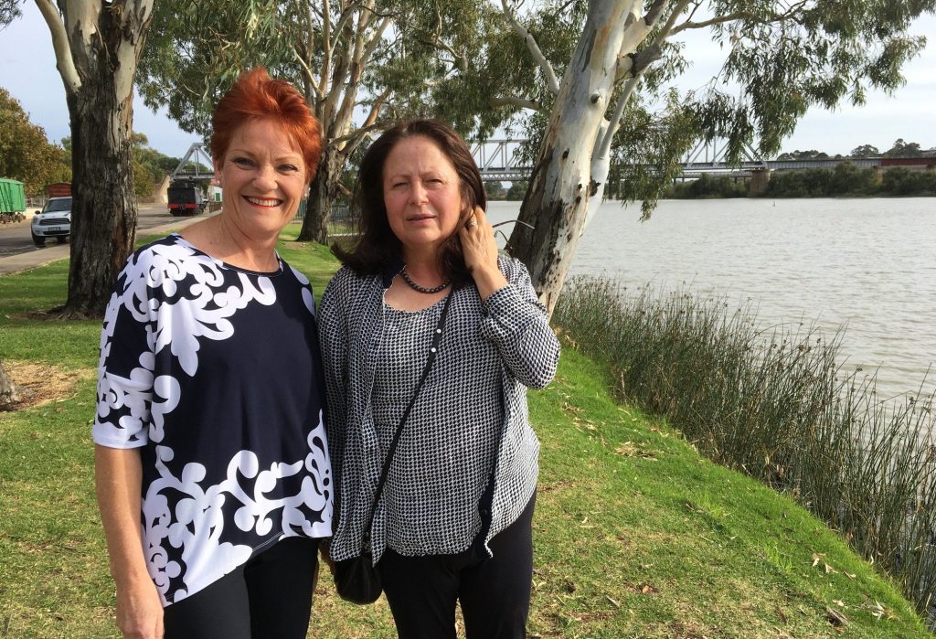 a redheaded woman in a navy and white shirt standing next to a brunette woman wearing grey by a lake