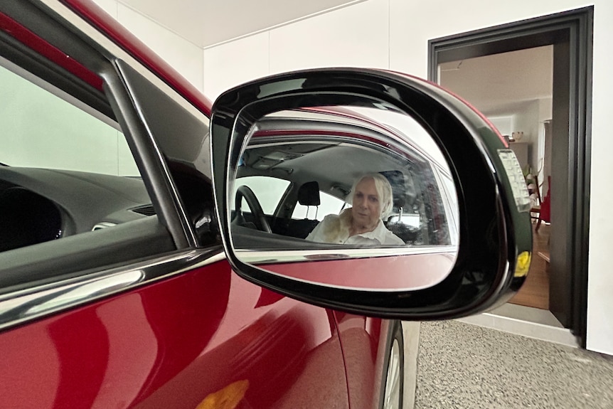 A woman's face reflected in the side mirror of a maroon coloured car.
