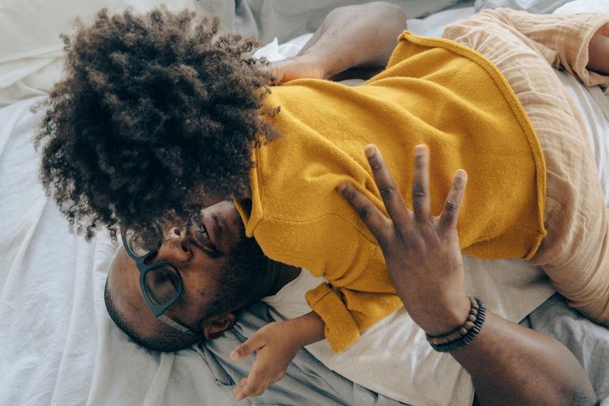 Dad playing with young boy on bed.