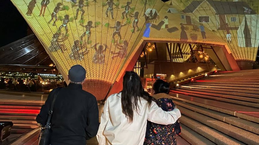 Three people look at an art projection on the Sydney Opera House.