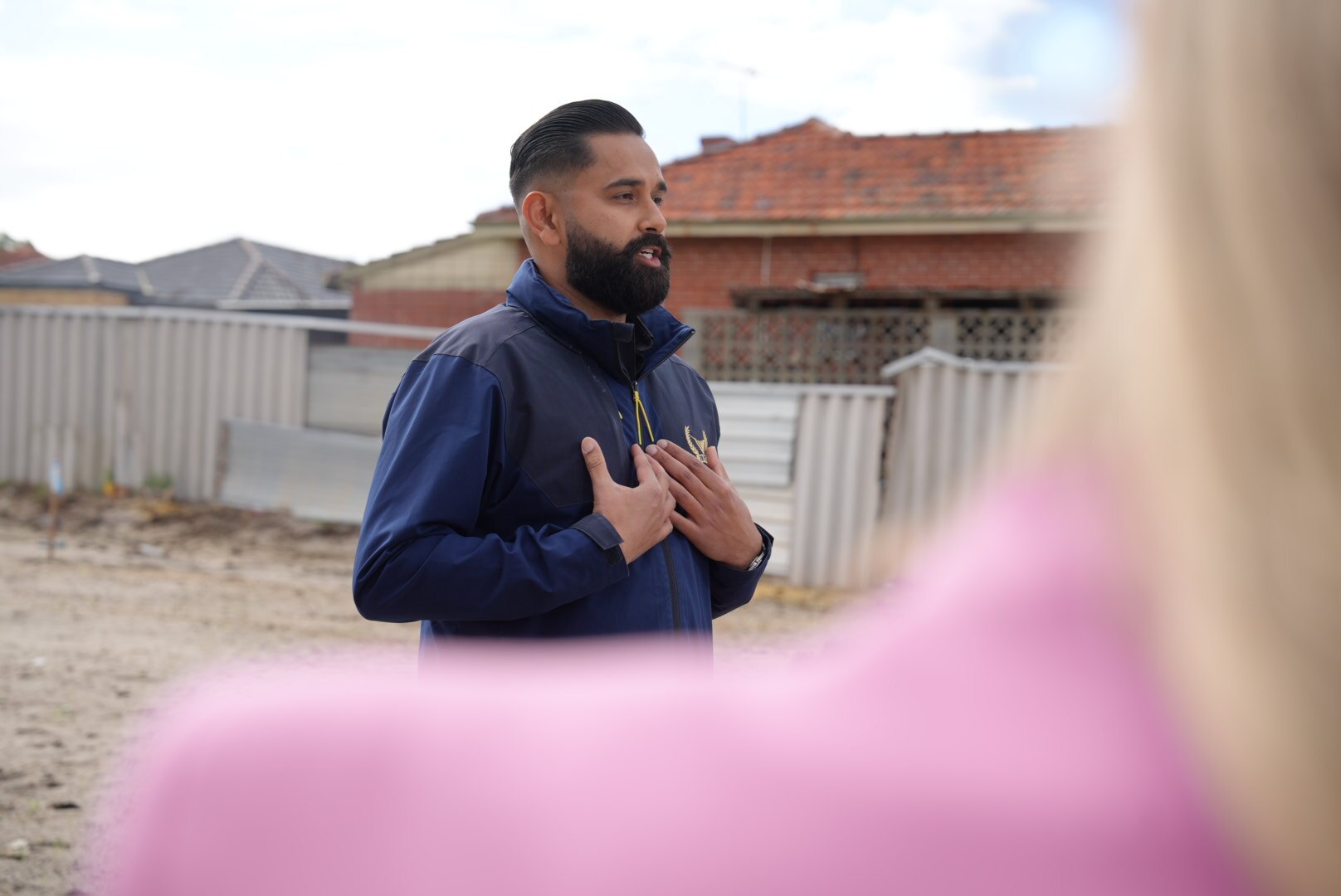 Un hombre con una chaqueta azul marino hablando, sosteniendo sus manos en el pecho. 