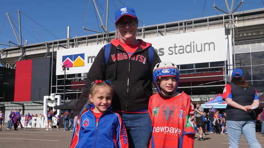 A smiling mother and her kids outside a stadium, all of them dressed in Newcastle Knights gear.