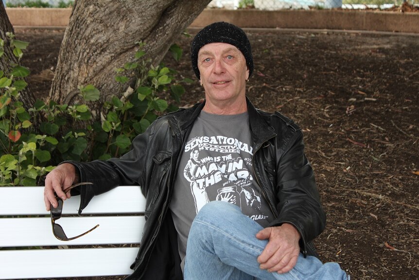 middle aged man sitting on a park bench looking relaxed.