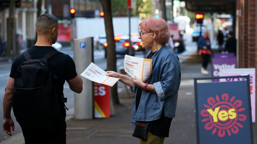 A woman with pink hair hands out info at a pre-polling station