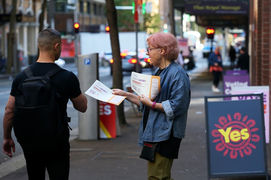 A woman with pink hair hands out info at a pre-polling station