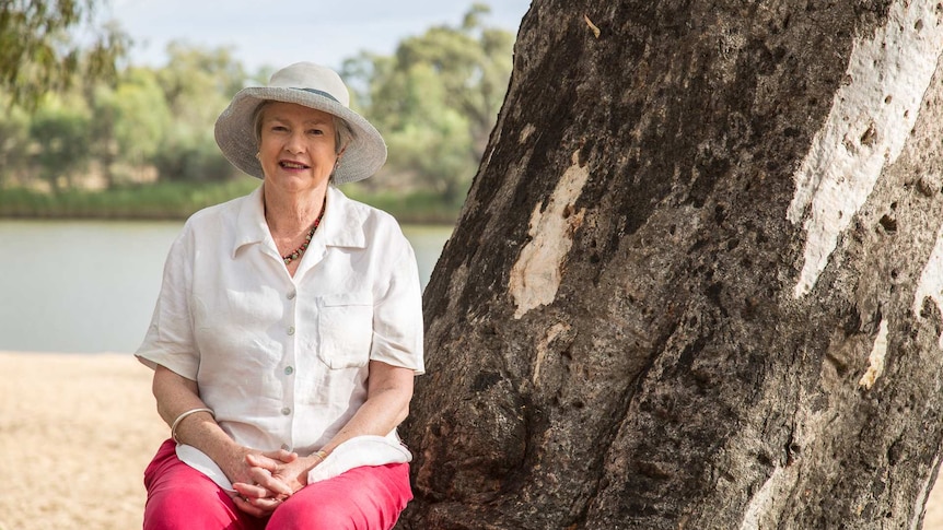 A woman sitting on the roots of a eucalyptus tree.