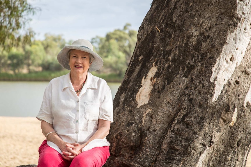 A woman sitting on the roots of a eucalyptus tree.