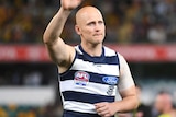 Gary Ablett looks downbeat while waving to the crowd. Geelong players can be seen lined up behind him