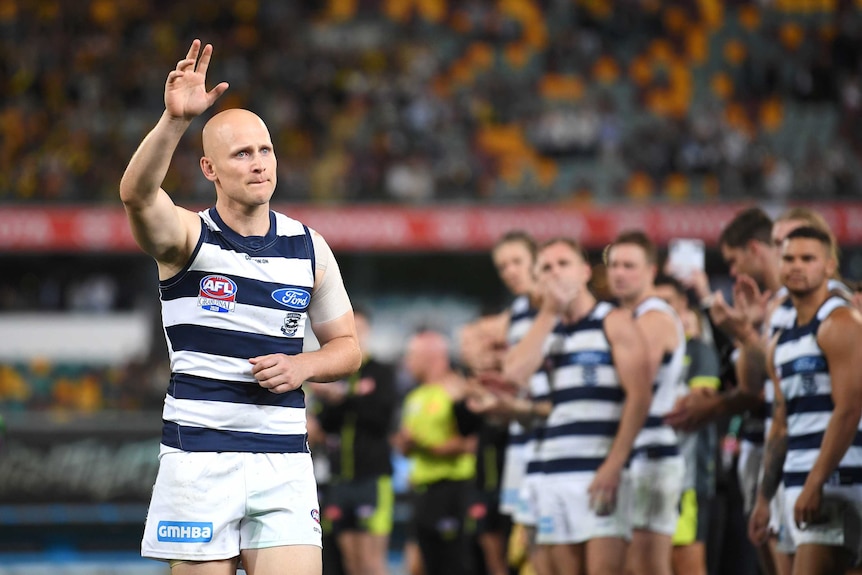 Gary Ablett looks downbeat while waving to the crowd. Geelong players can be seen lined up behind him