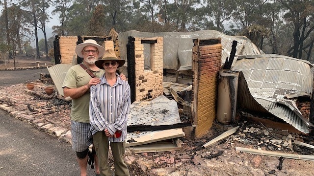A man and a woman standing outside their burnt down home near a forest
