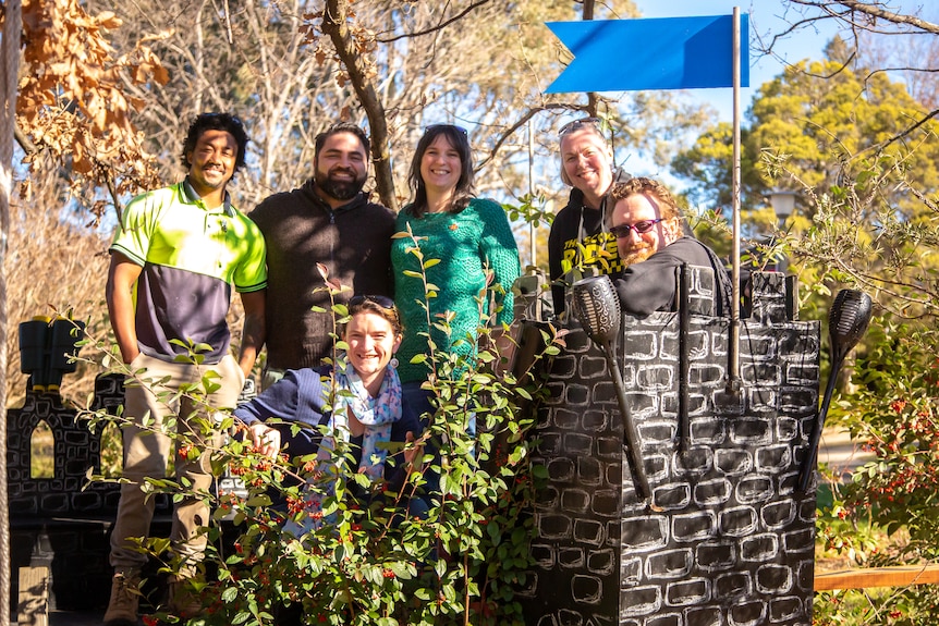 Six adults smile and pose at a children's playground.