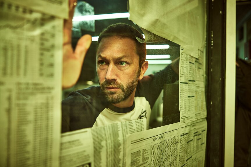 Richie looks through a window that's been covered by newspapers.