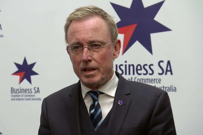 A man in a suit in front of a white background with a blue star