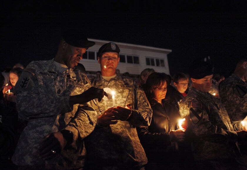 Soldiers wearing green uniforms light candles at night.