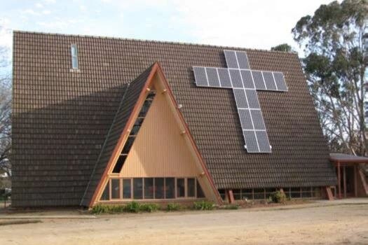 A large christian cross made of solar panels sits on the roof of a church