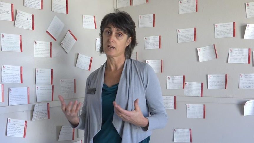 Woman stands in front of wall of many small hand-written notes