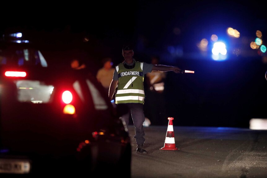 A policeman in a high-visibility vest directs traffic with a torch in darkness.