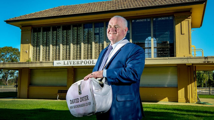 Bookmaker David Dwyer holds his bag and smiles for the camera.