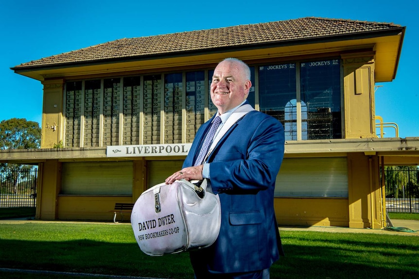 Bookmaker David Dwyer holds his bag and smiles for the camera.