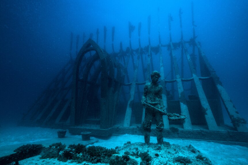 An underwater sculpture of a gardener in front of a greenhouse structure
