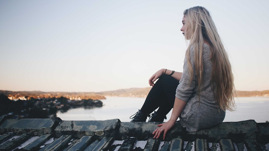 Young woman with long blonde hair sitting looking out to sea.