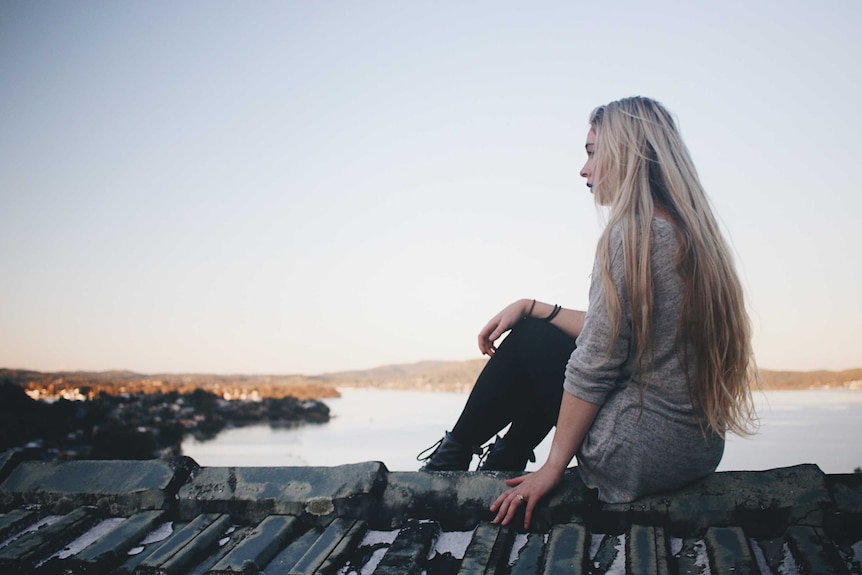 Young woman with long blonde hair sitting looking out to sea.