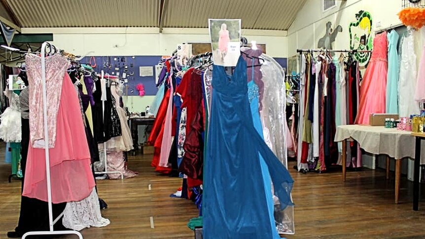 Lots of racks of dresses in a community hall.