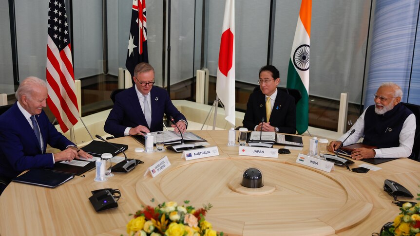 Joe Biden, Anthony Albanese, Japan's Fumio Kishida and Narendra Modi sit at a table in front of their countries flags.