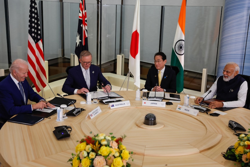 Joe Biden, Anthony Albanese, Japan's Fumio Kishida and Narendra Modi sit at a table in front of their countries flags.