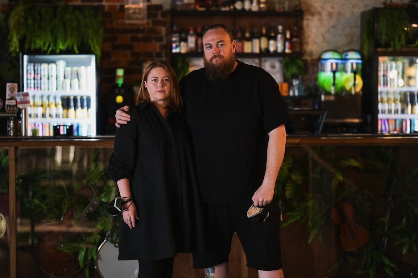 A man with his arm around a woman in a dark bar.