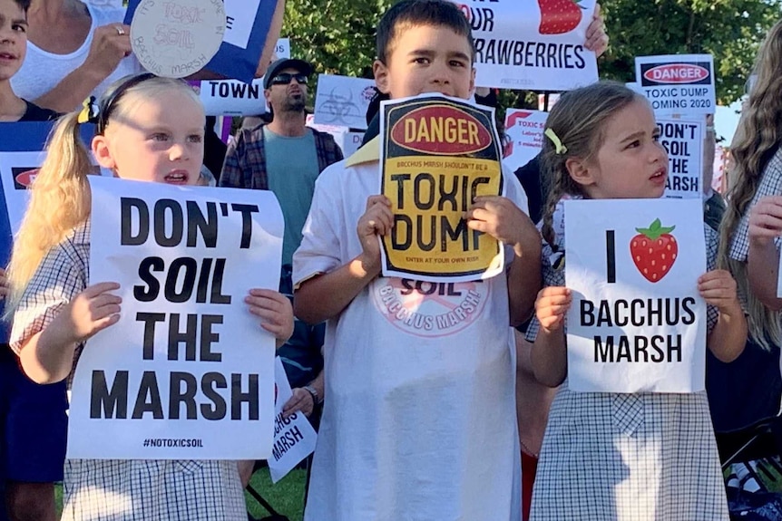 A group of children and an adult hold up signs protesting against a toxic dump.