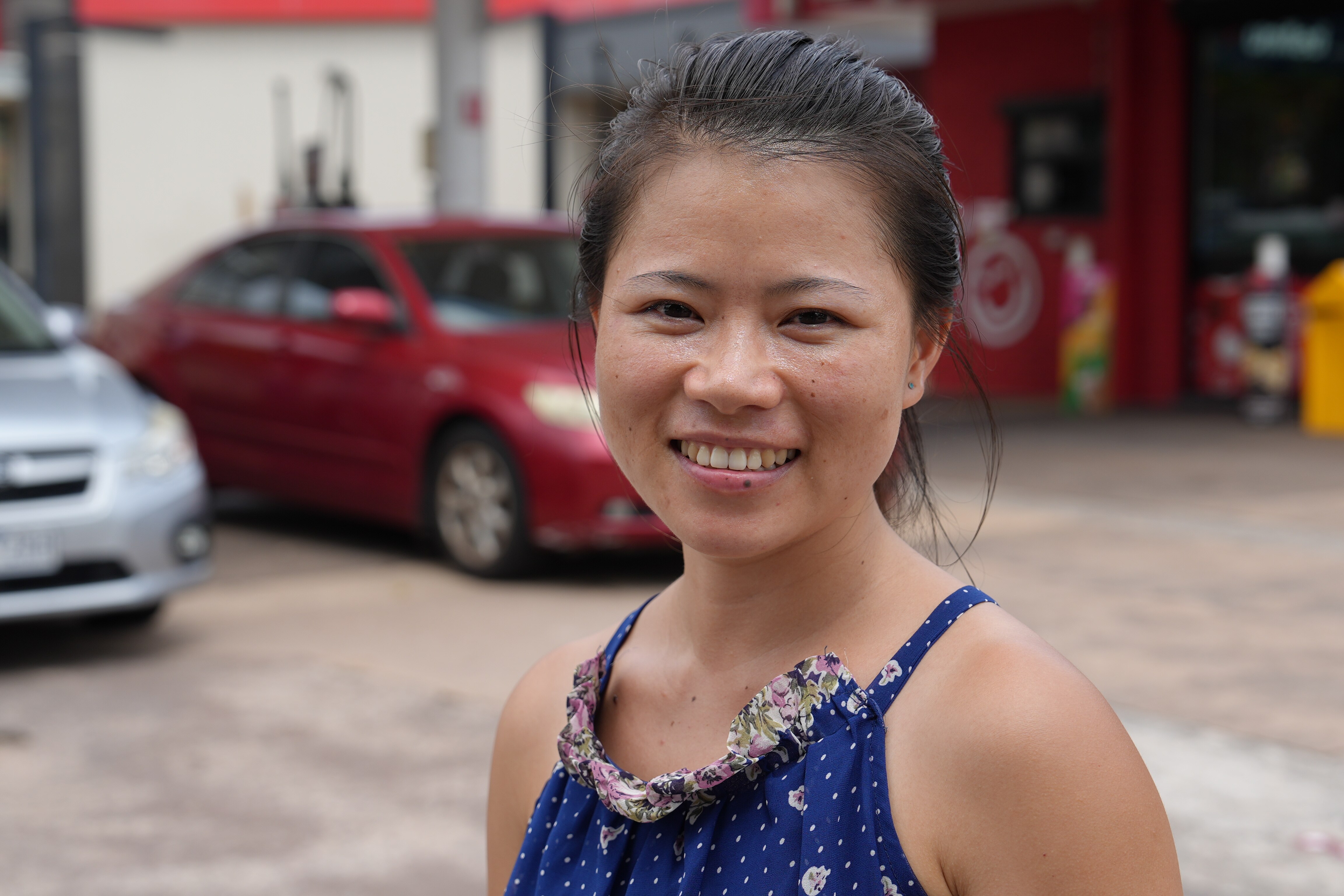 A portrait shot of a young woman in a blue dress standing in front of cars in a carpark.