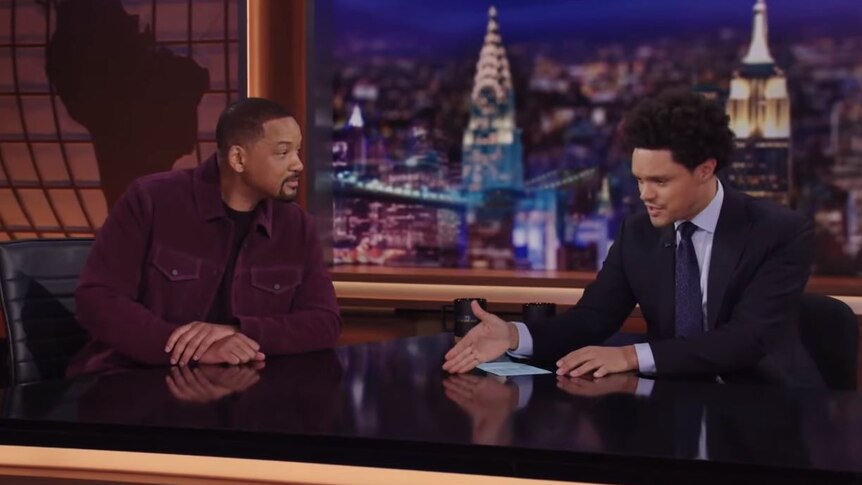 A screen grab of Will Smith and Trevor Noah sitting in a television studio at a desk