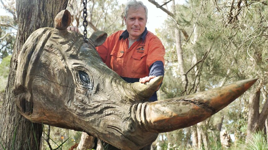 Darrel Radcliffe stands behind a sculpture of a rhino head.